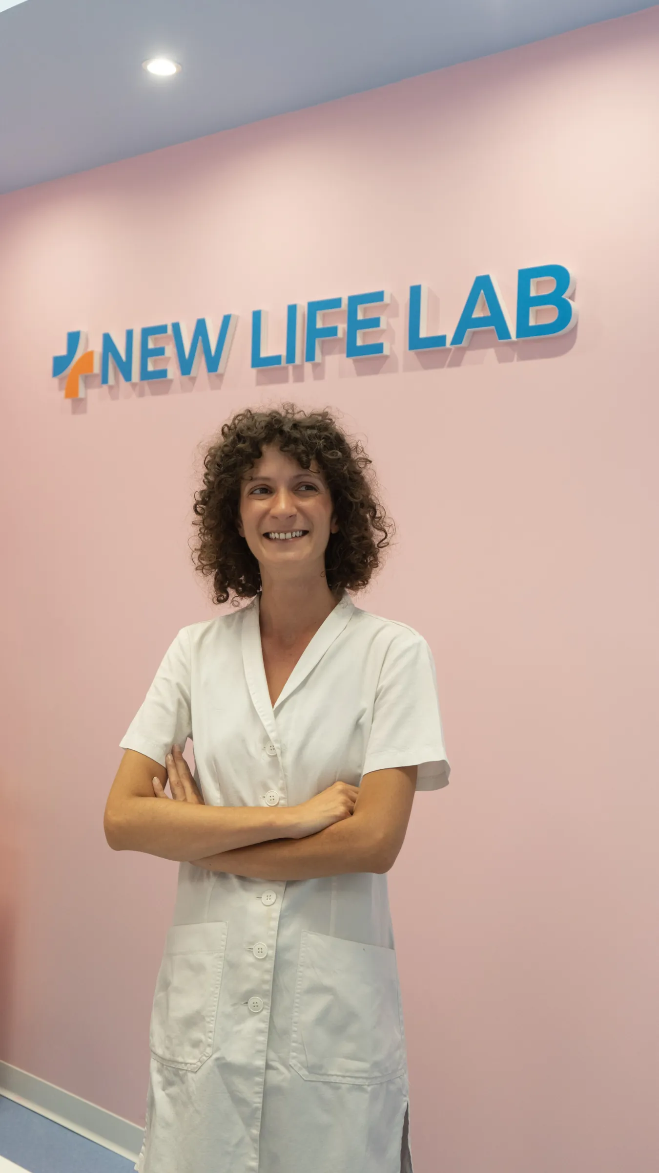 Una biologa del laboratorio, sorridente, davanti alla parete con il logo New Life Lab
